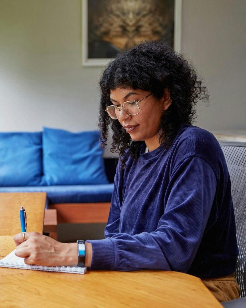 A woman taking notes at her desk beside a laptop