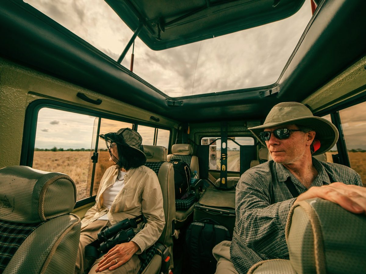 Two travelers sitting in a safari vehicle, looking out at the bush